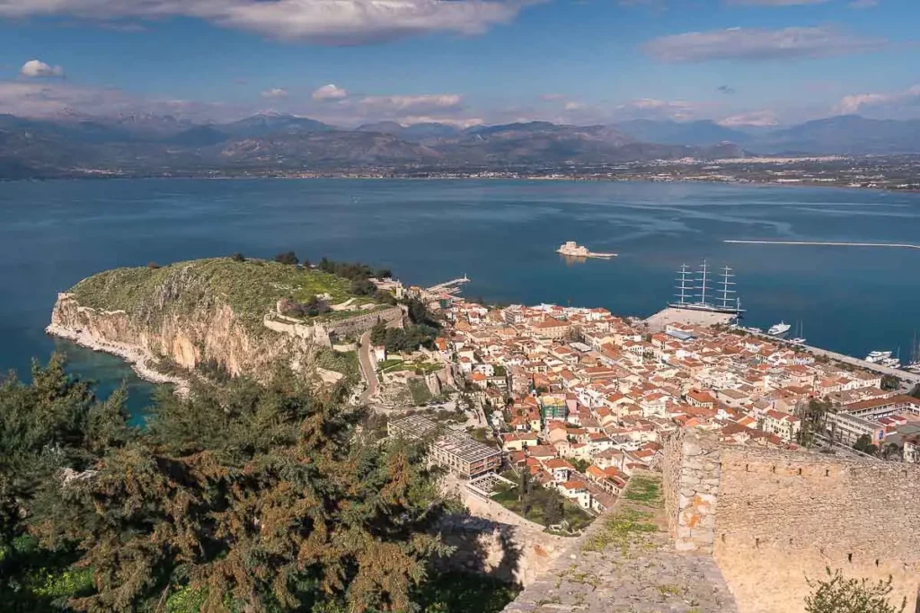 Argolis Road Trip in Greece- view over blue ocean, orange roofed houses and green shrubs
