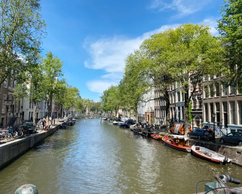 3 day Itinerary for Amsterdam, Canal Cruise- large canal, green trees, boats, tall dutch houses, Amsterdam