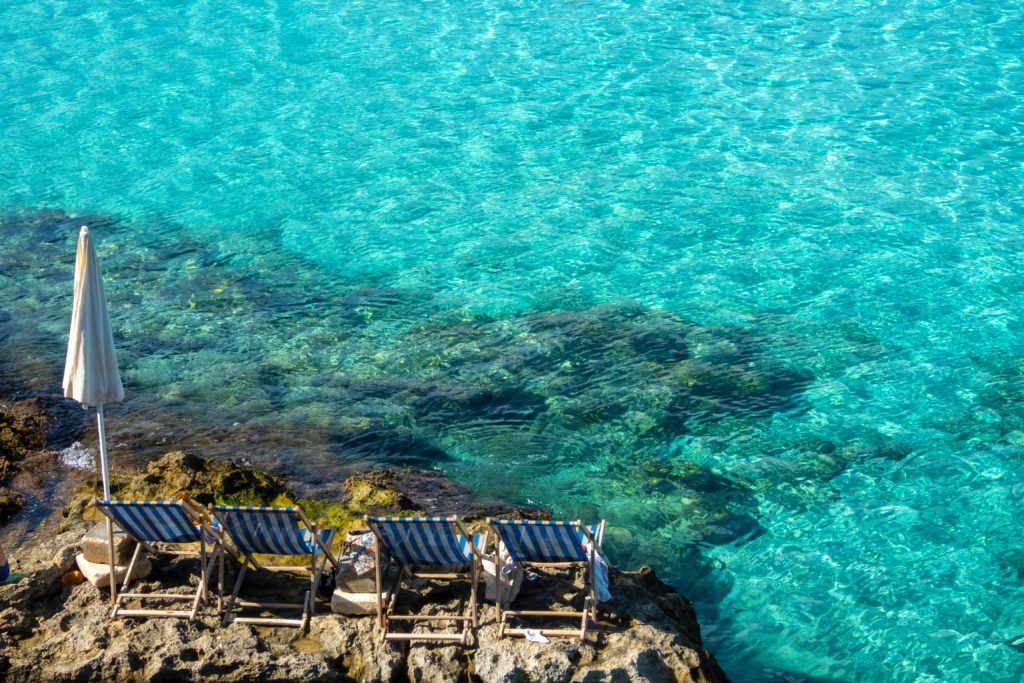 Full-Day Private Boat Charter in Malta, Gozo & Comino, blue water, deckchairs, grey cliff edge into water, Malta