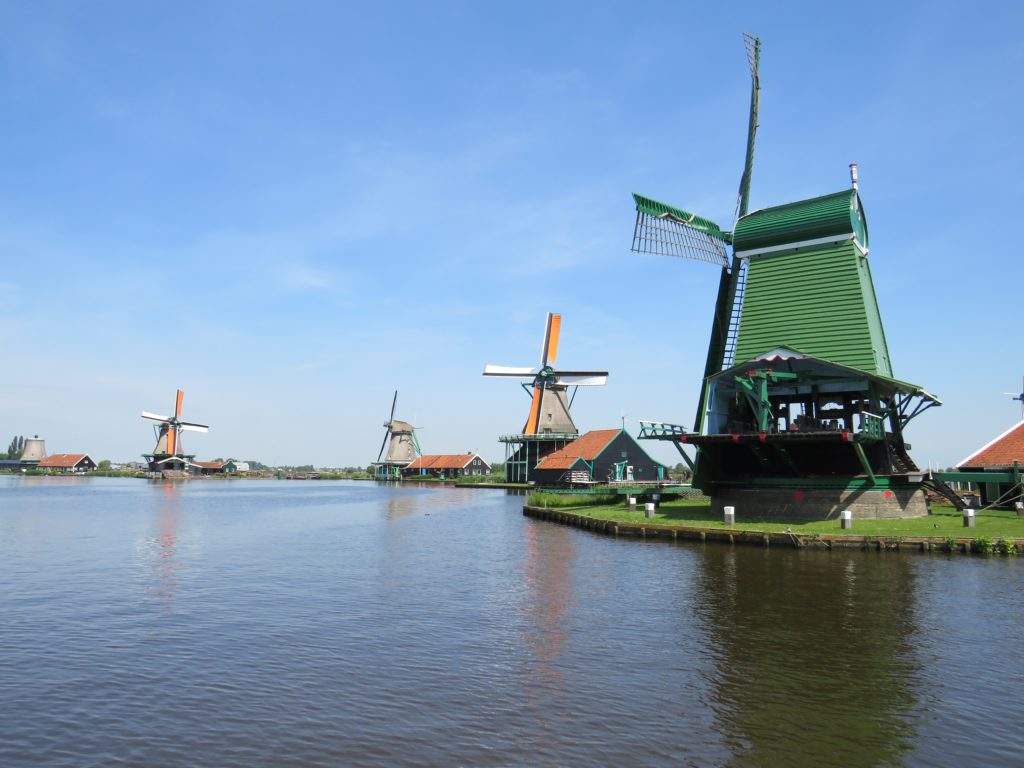 Zaanse Schans is a great day trip from Amsterdam during a 3 day trip- green windmill, brown windmills on green grass, surrounded by blue water in the Netherlands