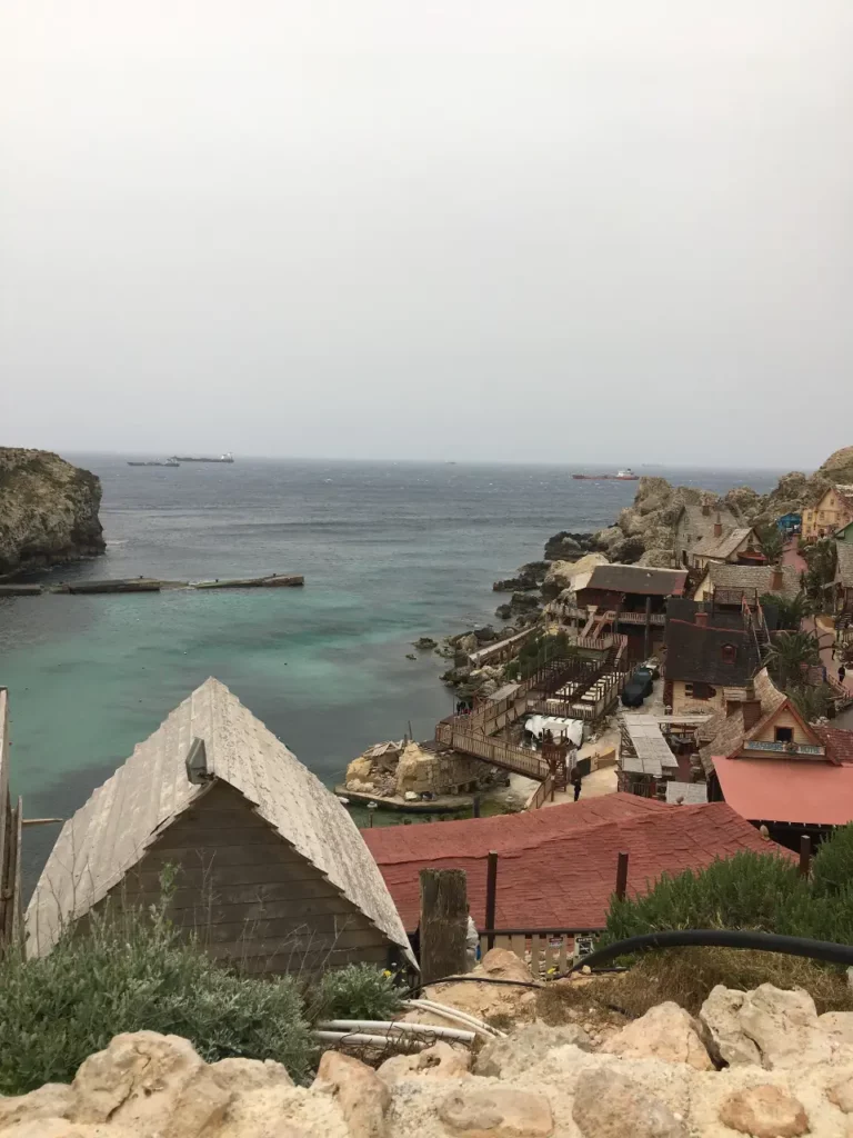 best private boat trips in Malta to see Popeyes Village- blue waters, red roofed wood houses, overlooking Anchor bay, Malta