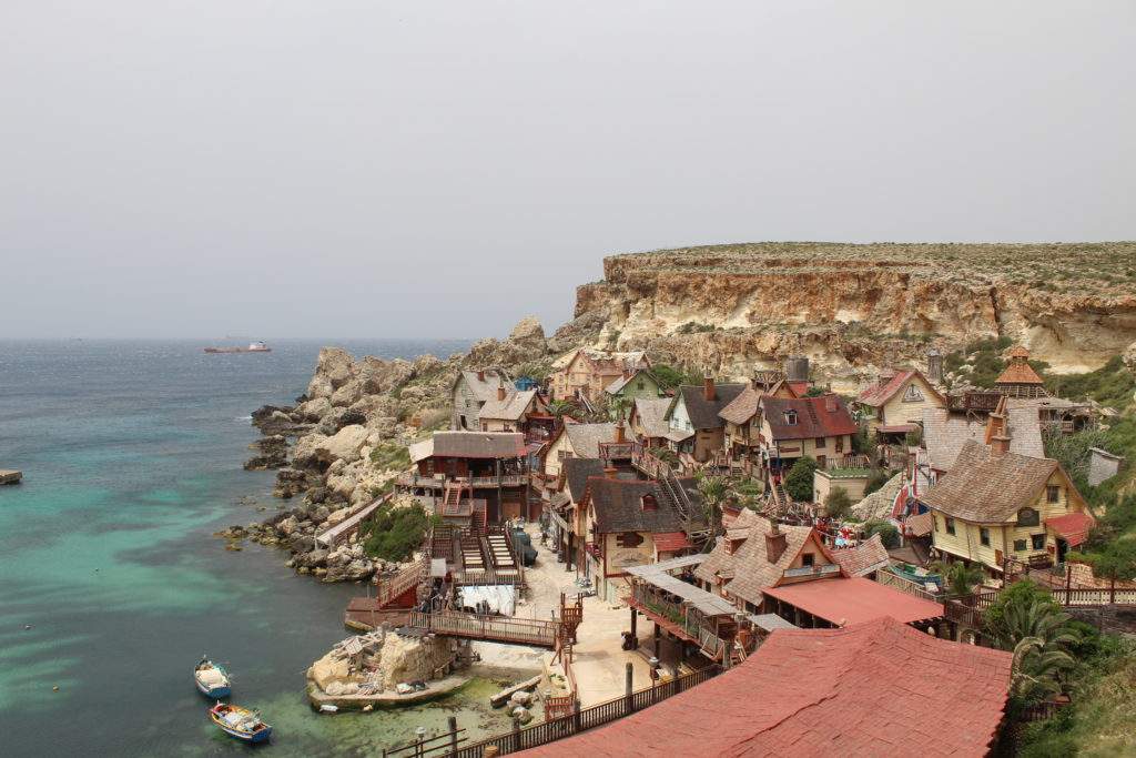 how to get to popeye village by car- cliff view over popeye village, red roof building, wooden buildings, blue water