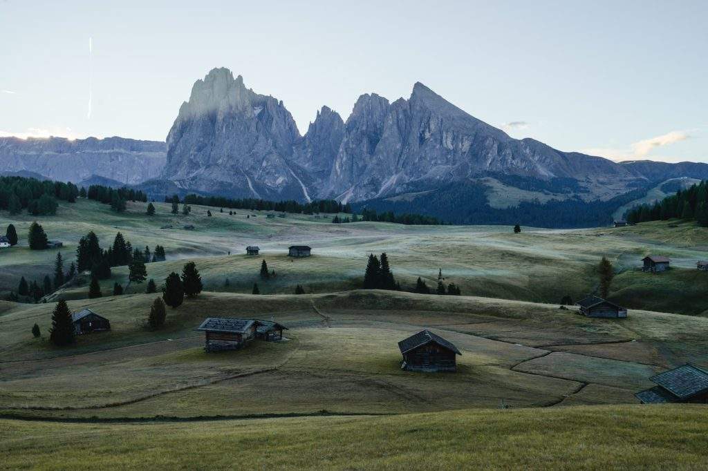 Italy Helicopter Tours Over The Dolomites- green fields, wood houses, mountain range