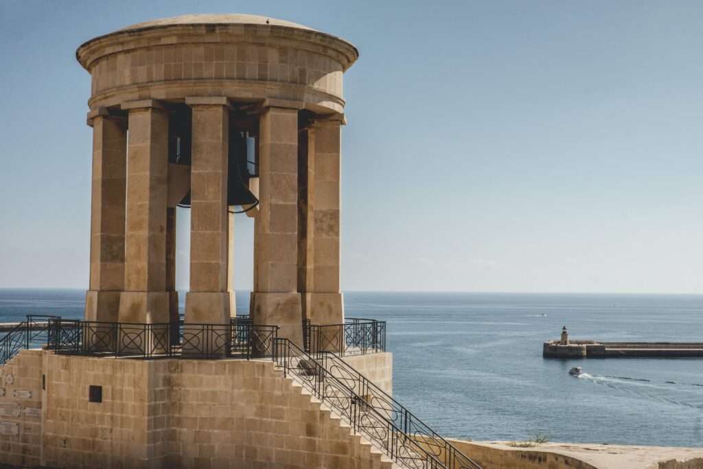 best Malta walking tours to explore Valletta- blue waters, boat in distance, tall sand coloured historical building