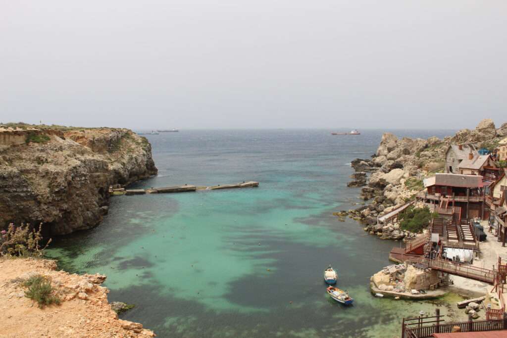 Best Private Tours In Malta- Popeyes Village- Blue waters surrounded by yellow cliffs and red and blue coloured roofs in Malta
