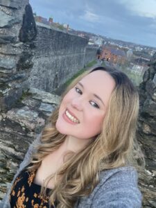 blonde girl smiling at camera with Derry City Walls in the background