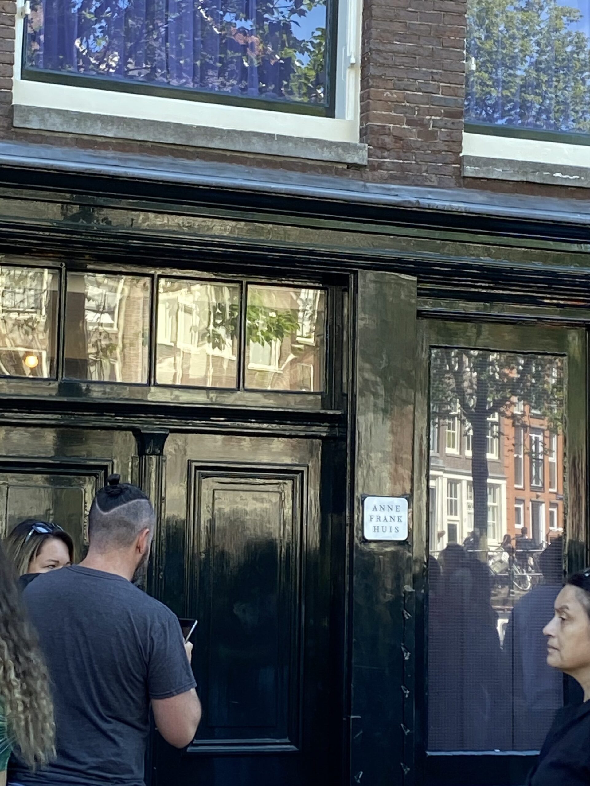 Crowds outside the black door and brown building with the gold sign saying "Anne Franks House" in a street in Amsterdam