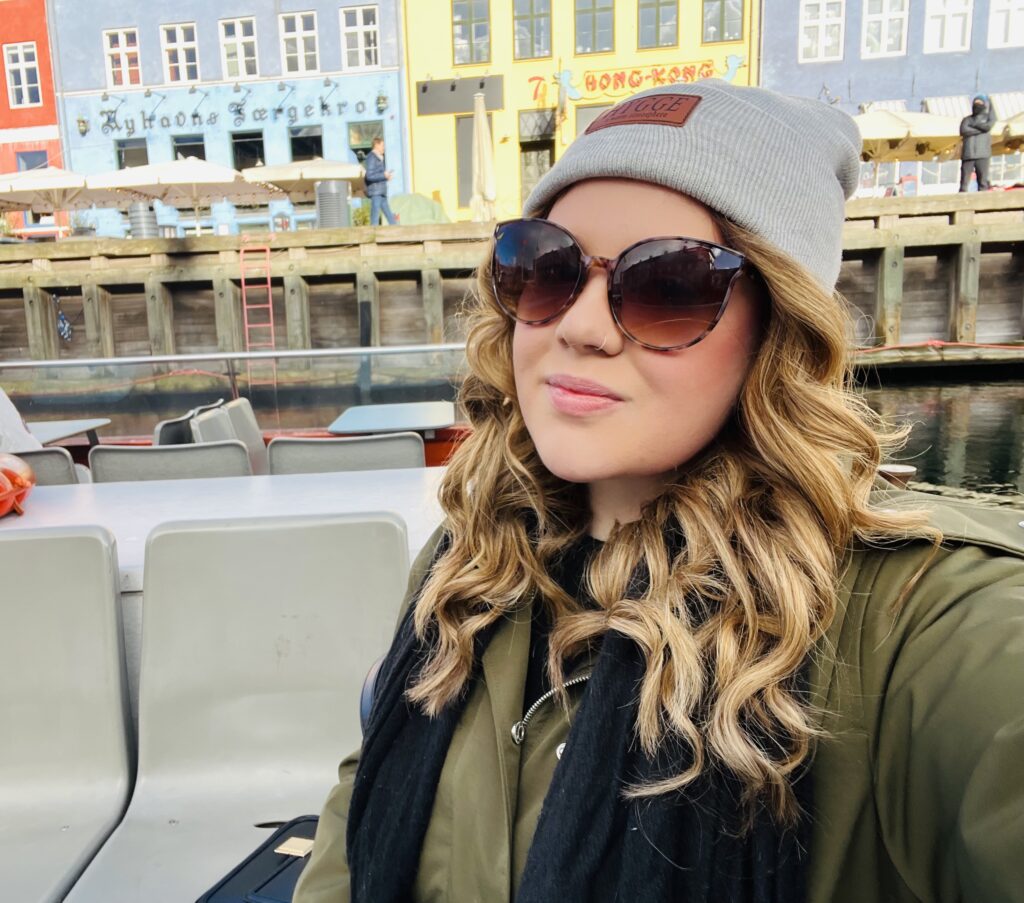 Girl with grey hat and sunglasses sat on a boat cruise infront of the colourful houses in copenhagen- wouldnt have been able to find the location without an e-sim!
